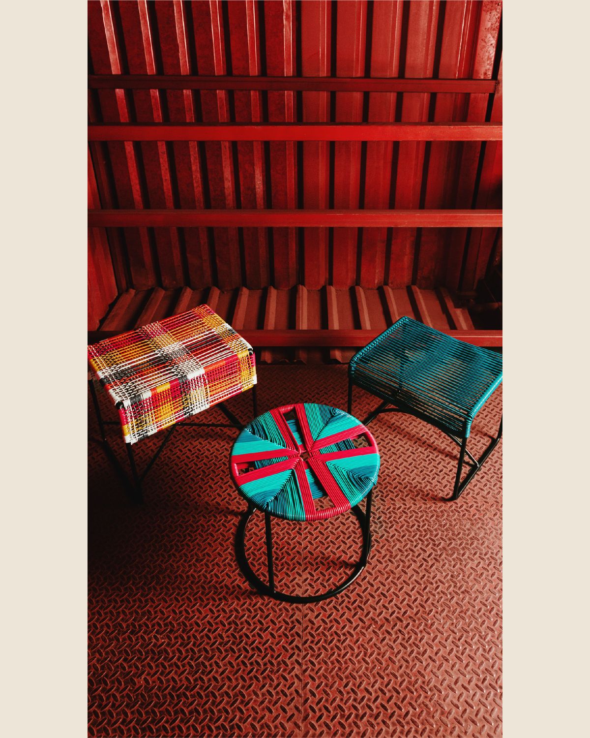 Dos bancos tejidos y una mesa redonda de tapa multicolor sobre un piso de lámina antiderrapante roja, bajo un techo de vigas del mismo rojo