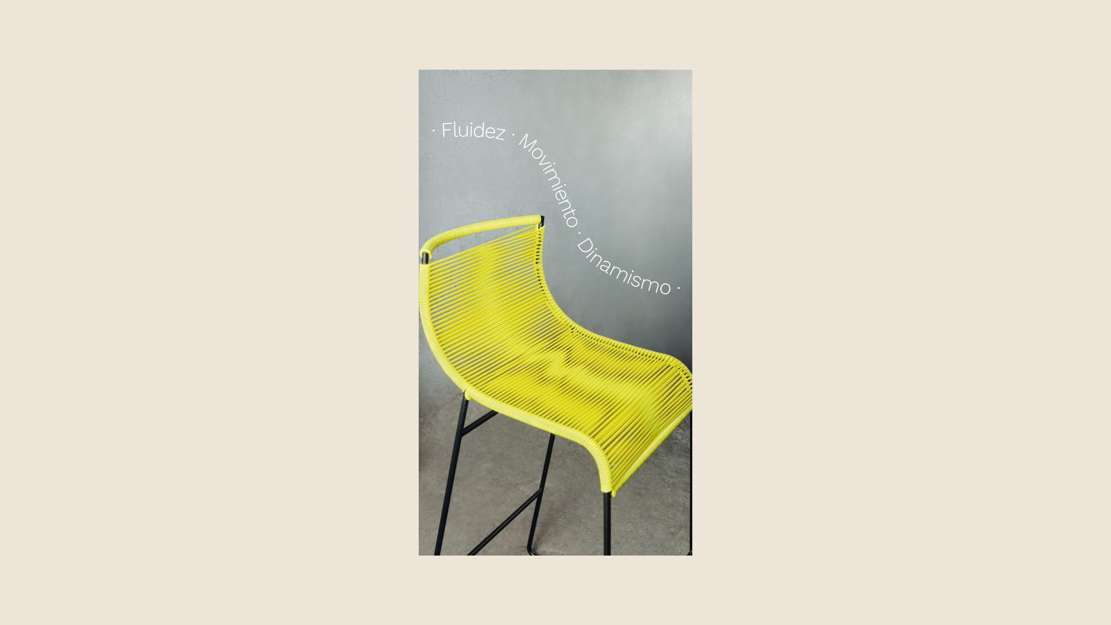 Pieza de campaña de Akele: una silla de tejido amarillo con estructura metálica negra fotografiada contra un muro de concreto, con las palabras «Fluidez · Movimiento · Dinamismo» en vertical al costado