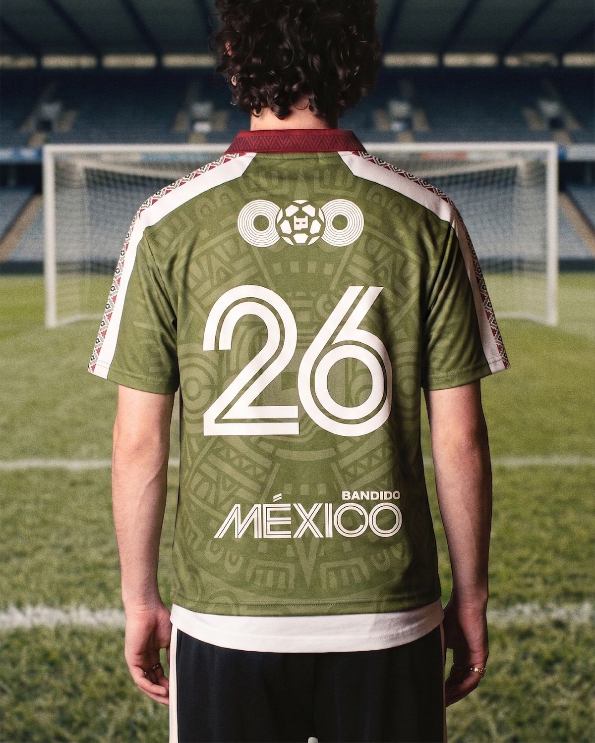 Una persona de espaldas, en la cancha de un estadio vacío, lleva puesto el jersey verde con el 26 y MÉXICO en la espalda y franjas blancas en las mangas