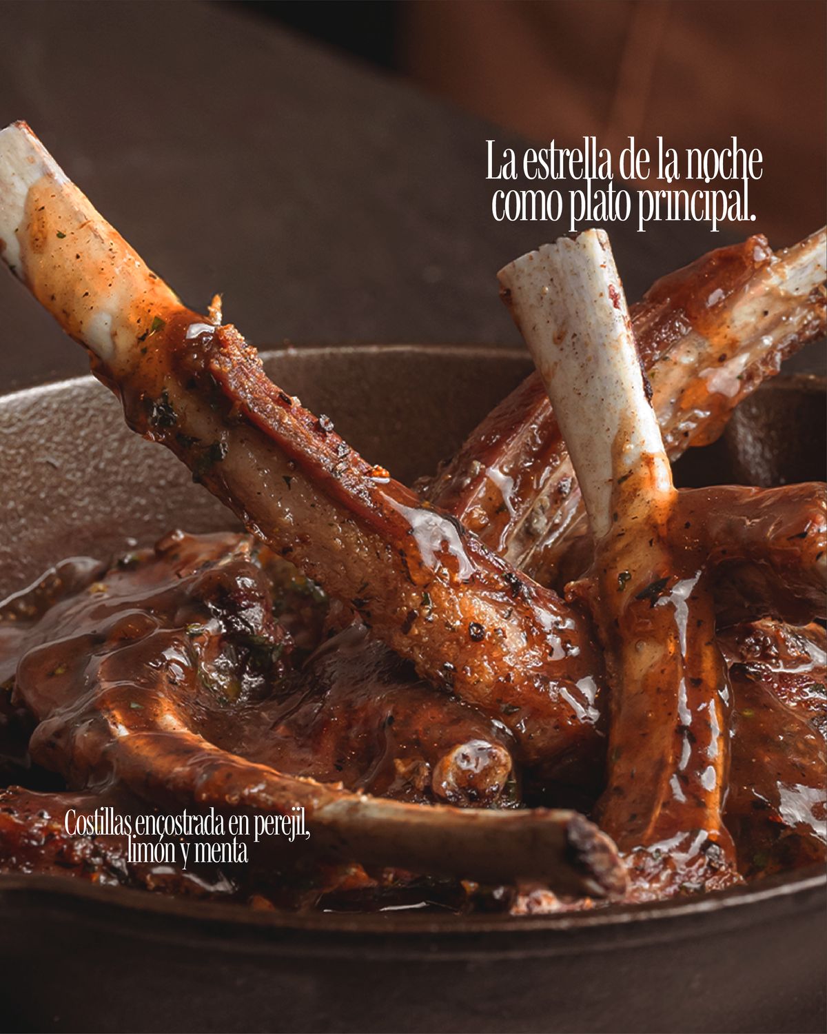 Primer plano de costillas glaseadas con los huesos al aire en una cazuela de hierro sobre fondo oscuro, con los textos en serif condensada «La estrella de la noche como plato principal» y «Costillas encostrada en perejil, limón y menta»