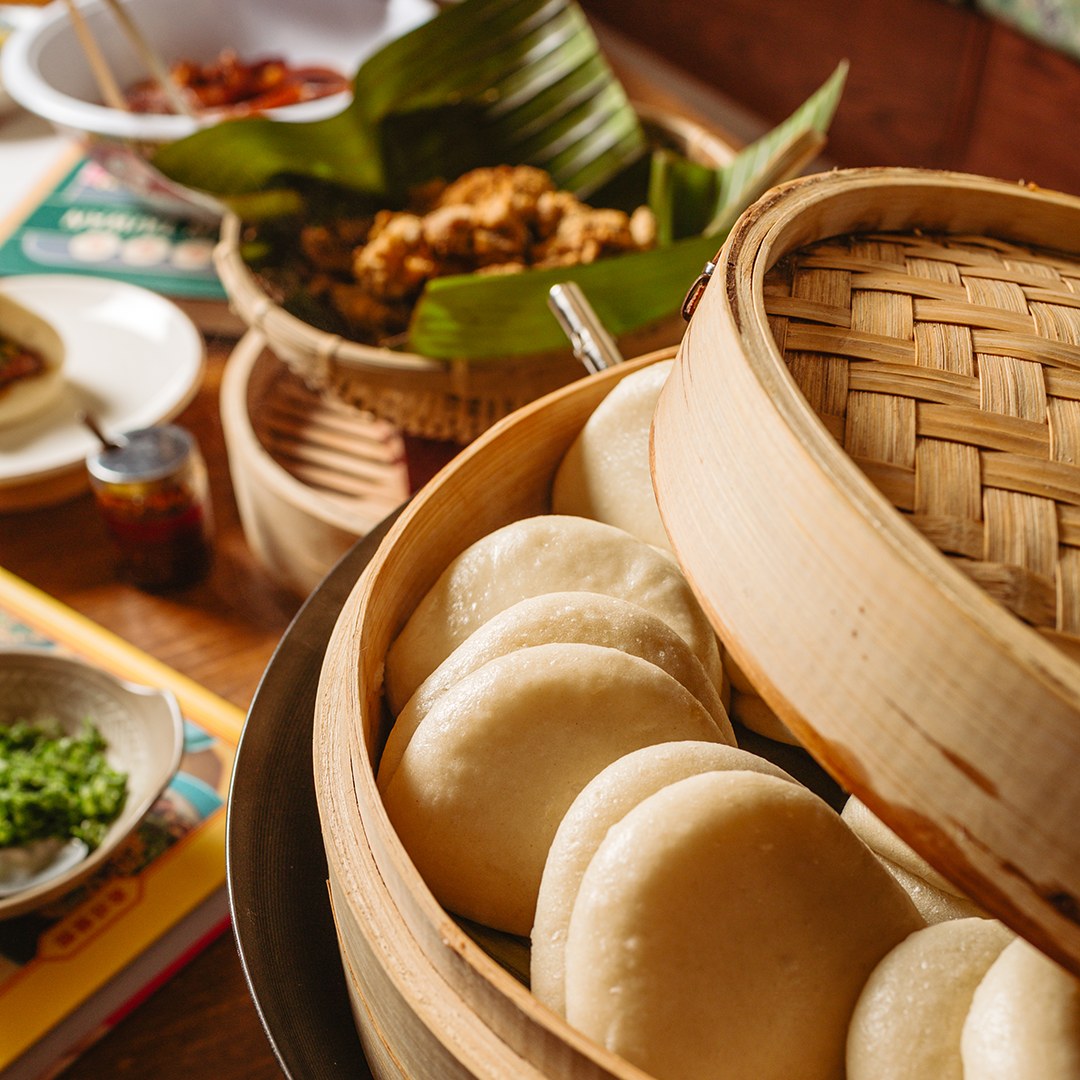 Baos en una vaporera de bambú con platos taiwaneses al fondo