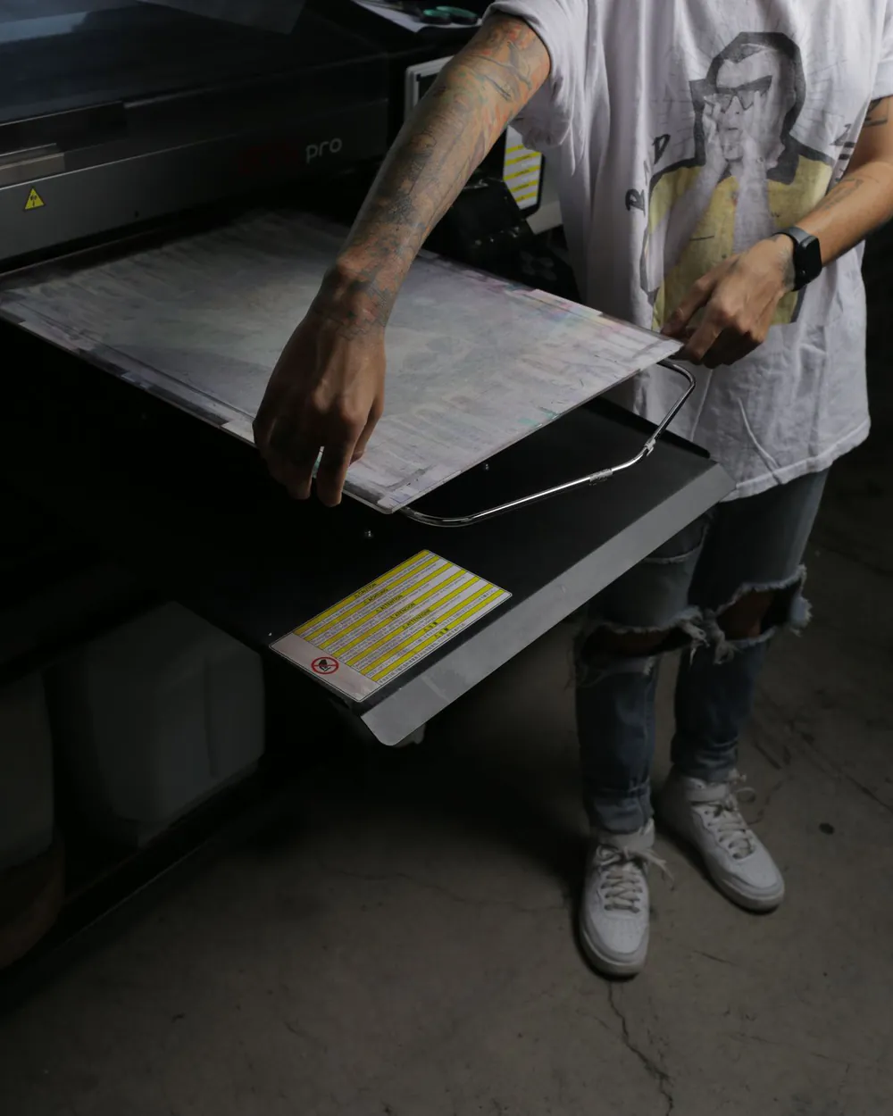En el taller de Kong, un brazo tatuado desliza la base de una impresora textil GTX pro, la máquina que imprime directo sobre la prenda