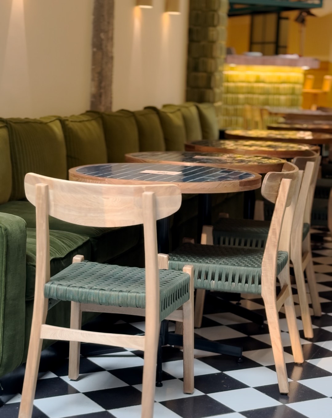 Interior de FIGA con mesas de madera, sillas tejidas verdes y piso ajedrezado