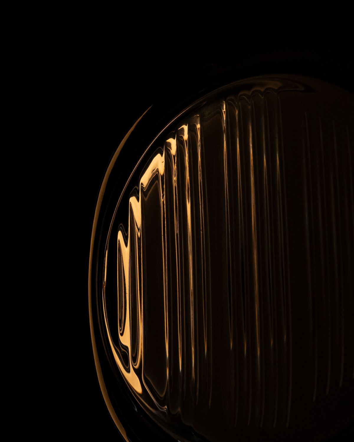 Detalle de un difusor de vidrio estriado encendido en luz cálida, con el borde curvo del vidrio brillando contra el negro