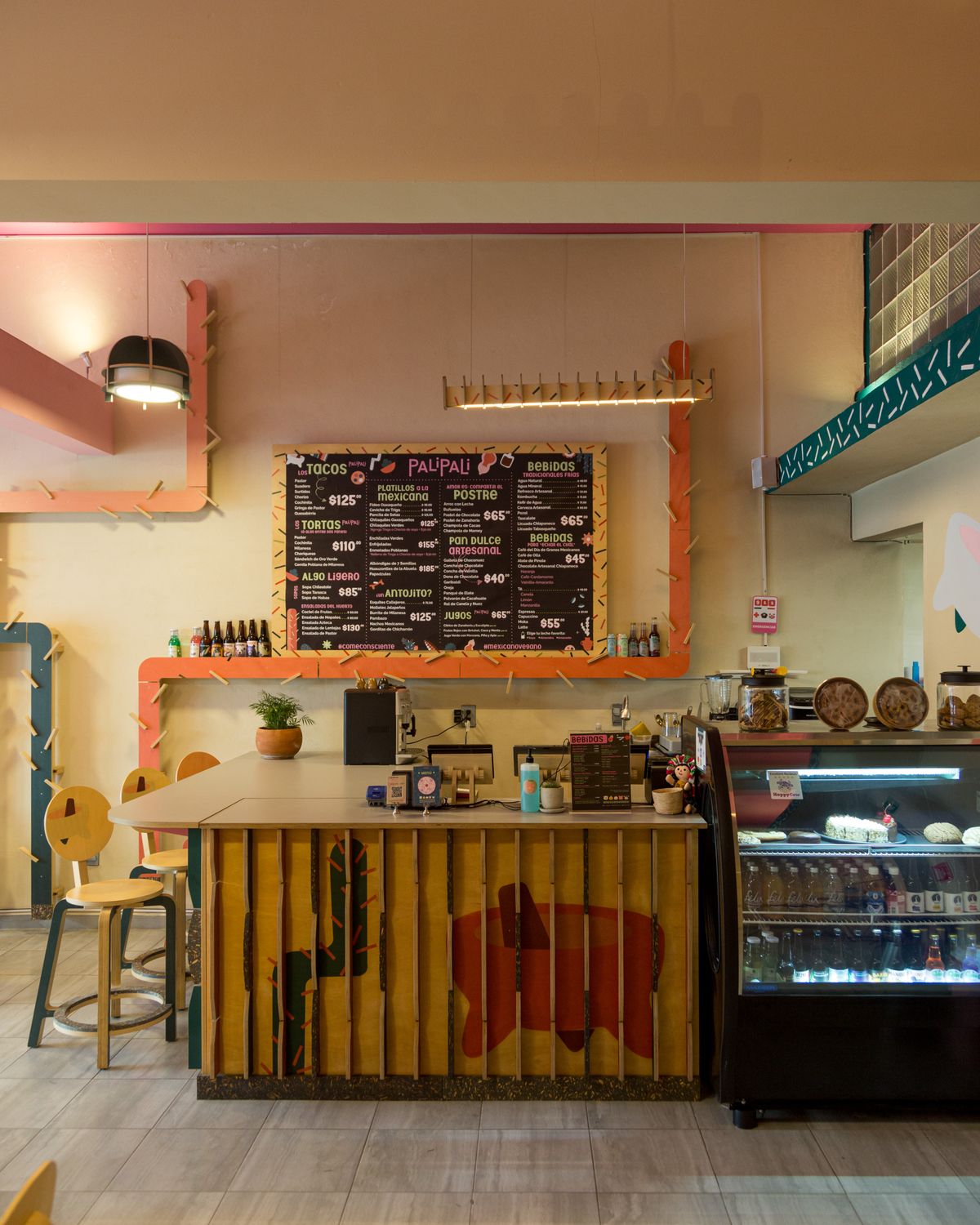 Barra de madera con frente de tablas y una vitrina refrigerada, bajo un pizarrón con el menú y el mismo tubo de colores enmarcándolo