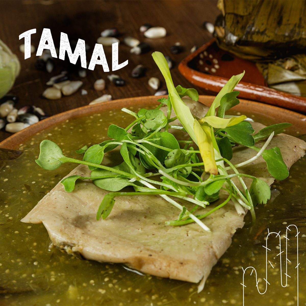 Plano cerrado de un tamal sin hoja bañado en salsa verde y coronado con germinados, en un plato de barro, con el título «TAMAL» en letras blancas y semillas blancas y negras esparcidas al fondo