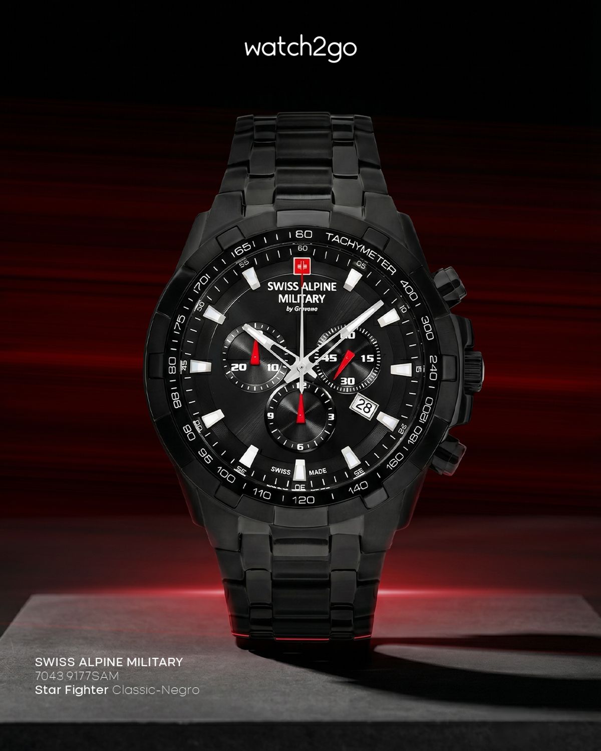 Reloj cronógrafo negro con detalles rojos sobre un pedestal oscuro, iluminado desde arriba, con el logotipo de watch2go en la parte superior
